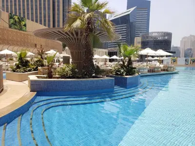 a large swimming pool with palm trees and umbrellas at Deluxe 1 BR At Address Apartments Marina Mall by Primevanguard in Dubai