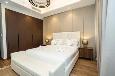 a white bedroom with a large white bed and a bench at Spacious Luxe 2BR in Dubai - With Pool and Gym in Dubai