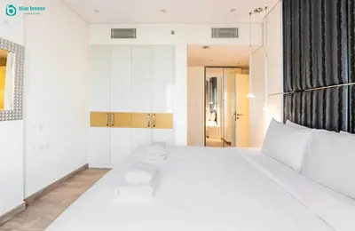 a bedroom with a large white bed with white furniture at Blue Breeze - Stunning 1BR with Canal & Pool Views in Dubai