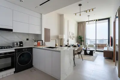 a kitchen with white cabinets and a living room at GuestReady - New Gem | JVC | Binghatti Gardenia in Dubai