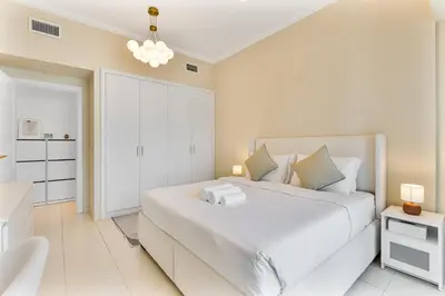 a white bedroom with a large white bed and a chair at Upmarket - 1BR - Canal View - 9 MIN Dubai Mall in Dubai