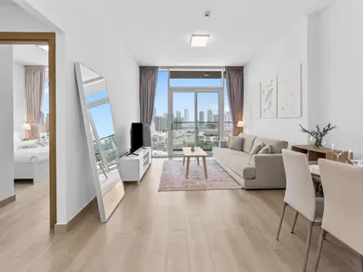 a white living room with a couch and a tv at Bright 1 Bedroom Apartment with JVC open view in Dubai
