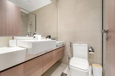 a bathroom with a toilet and two sinks and a mirror at Stylish 1BR with Netflix Pool & Gym Access in Dubai