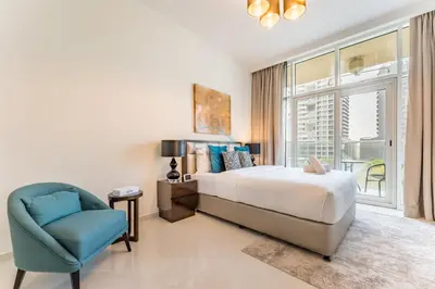 a bedroom with a bed and a chair and a window at Furnished Studio Near Circle Mall, Close to Parks, Jogging Tracks, Bus Stops And Grocery Stores - Damac Ghalia, JVC by Deluxe Holiday Homes in Dubai