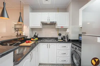 a kitchen with white cabinets and a dishwasher at Vogue Sports City Elite near First Avenue Mall, One Bedroom Apartment with Balcony and Vibrant Community View, Access to all Amenities in Dubai