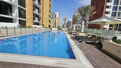 a large swimming pool with chairs and an umbrella at Azizi Riviera Luxury Studio with Grand Balcony in Dubai