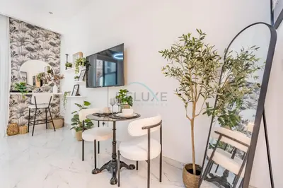 a table and chairs in a room with plants at Just Steps Away from Circle Mall, Right Beside a Park, Near Restaurants, Conveniently Close to a Bus Stop, Lumina Vista Residences, Jumeirah Village Circle by Deluxe Holiday Homes in Dubai