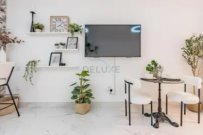 a living room with a tv and a table and chairs at Just Steps Away from Circle Mall, Right Beside a Park, Near Restaurants, Conveniently Close to a Bus Stop, Lumina Vista Residences, Jumeirah Village Circle by Deluxe Holiday Homes in Dubai