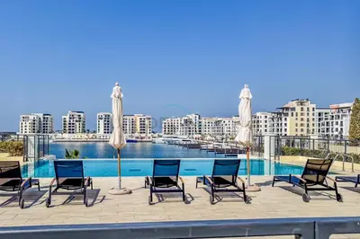 a group of chairs and umbrellas next to a swimming pool at Urban Beachside 2BR with a Glimpse of Burj Khalifa, Near Jumeirah Beaches, Short Drive to Mercato Mall, La Sirene Building 4, Jumeirah by Deluxe Holiday Homes in Dubai
