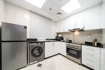 a kitchen with white cabinets and a washer and dryer at Bright and Stylish 2 Bed Home Opposite Circle Mall in Dubai