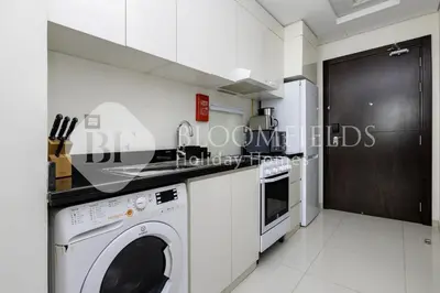a white kitchen with a washer and dryer at Bloomfields Elegant Stu Damac Ghalia in Dubai