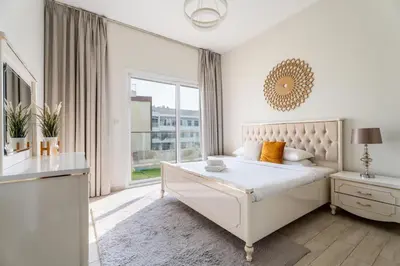 a white bedroom with a bed and a window at GuestReady – Relax Stay w Balcony & Pool View in Dubai