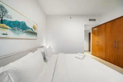 a white bedroom with a bed and a wooden cabinet at FIRST CLASS 3BR Stunning Burj Khalifa View in Dubai