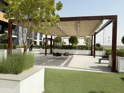 acovered patio with a table and chairs and grass at ASHRI HH Condo In Riviera Meydan in Dubai