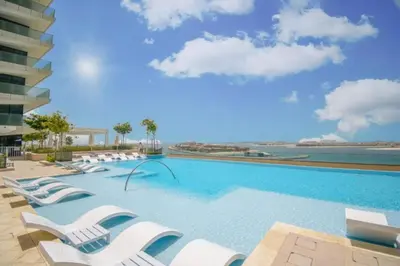 a large swimming pool with white lounge chairs at Beach Vista - One Bed with Infinity Pool Access in Dubai