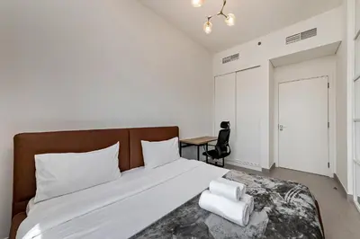 a bedroom with a bed with white sheets and a desk at Dubai Hills Cozy 1Br Golfville in Dubai