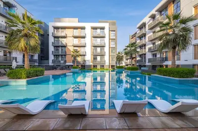a swimming pool with chairs in front of a building at Contemporary 2-BR at Belgravia Square JVC in Dubai