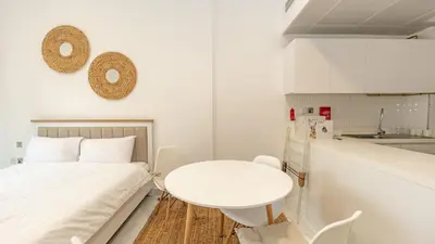 a white room with a white table and a kitchen at Cozy Studio in JVC in Dubai