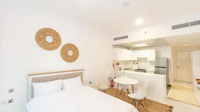 a white bedroom with a bed and a table and chairs at Cozy Studio in JVC in Dubai