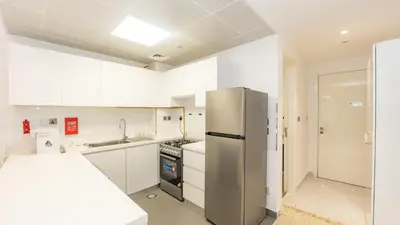a kitchen with white cabinets and a stainless steel refrigerator at Cozy Studio in JVC in Dubai