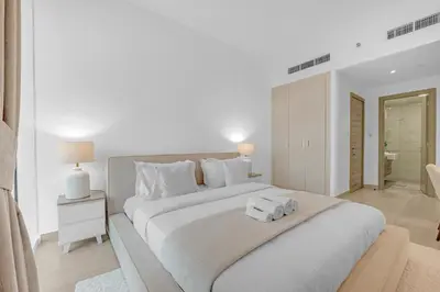a white bedroom with a large bed with two towels on it at Waves - Vibrant and Cozy 1BR Apt in JVC in Dubai