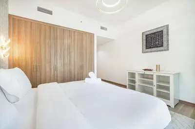 a white bedroom with a white bed and a wooden cabinet at Luxury 2BR w Floating Bed in Dubai Marina Sulafa 4404 in Dubai