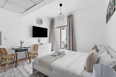 a white bedroom with a bed and a table and chairs at Beautiful Studio Prime location Pool & Gym in Dubai