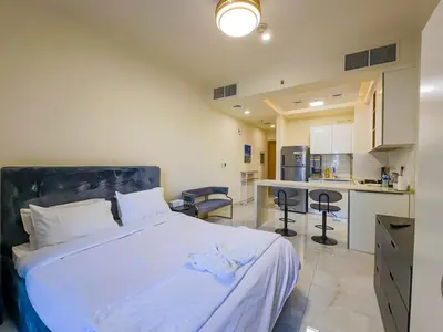 a bedroom with a white bed and a kitchen at Comfortable Studio Living in Dar Al Jawhara, JVC in Dubai