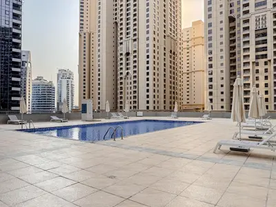 a pool with chairs and umbrellas on a building with tall buildings at The Smart Concierge - Marina Wharf in Dubai