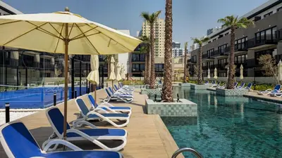 a row of lounge chairs with an umbrella and a pool at Brand New 2BR -Spacious in Dubai