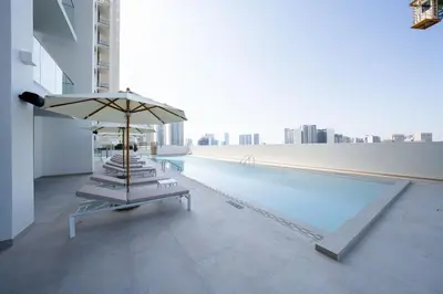 a pool with chairs and an umbrella on a building at Soft Toned 1BR Retreat with Pool, Gym and Parking! in Dubai