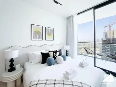 a white bedroom with a bed and a large window at JVC Retreat with Pool & Balcony in Dubai