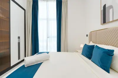 a bedroom with a bed with blue pillows and a window at Ahlan HH - Exclusive 2-BR Apartment in Opalz by Danube - Balcony with Mini Pool in Dubai