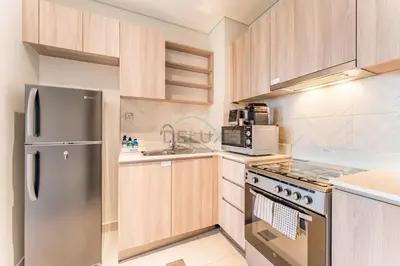 a kitchen with wooden cabinets and a stainless steel refrigerator at Steps from Dubai Hills Park, Walk to Dubai Hills Mall, 15-Minute Drive to Burj Khalifa and Dubai Mall, Sway Residences, Dubai Hills by Deluxe Holiday Homes in Dubai