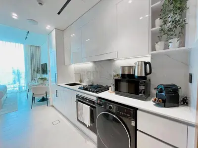 a white kitchen with a stove and a microwave at Lavish Studio Apt in Binghatti Azure - Pool & Gym in Dubai