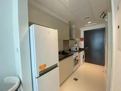 a kitchen with a white refrigerator and a black door at Modern DAMAC Hills Studio with Balcony, Gym & Pool in Dubai