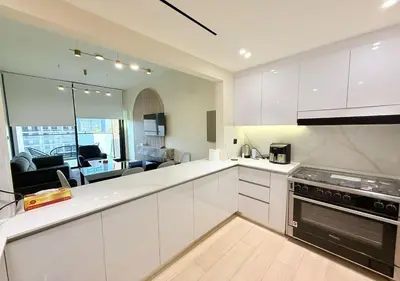 a kitchen with white cabinets and a living room at Binghatti Crescent Cozy 2 BR in Dubai