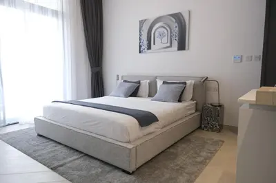 a bedroom with a large bed with white sheets and blue pillows at Beautiful Brand New Studio -Pool -Balcony -Parking in Dubai