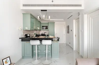 a kitchen with green cabinets and two white bar stools at 1BR Lagoon View Luxury Spa Retreat near Miracle Garden in Dubai