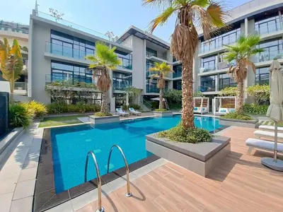a swimming pool with palm trees in front of a building at Oxford Boulevard - Vibrant Studio in JVC in Dubai