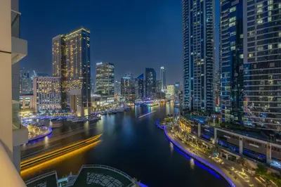 a city skyline at night with a river and buildings at Dubai Marina Waterfront Stay with Maid Room in Dubai