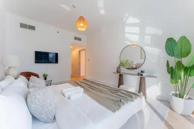 a white living room with a white couch and a mirror at Dubai Marina Waterfront Stay with Maid Room in Dubai