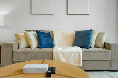 a living room with a couch with blue pillows and a table at TRPS - Farhad Azizi, Al Jaddaf - Premium 1BR, Furnished with Pool View in Dubai
