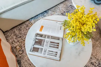 a table with a book and a vase of yellow flowers at Bella Casa - Luxury 1BR Apartment - Brand New Furniture in Dubai