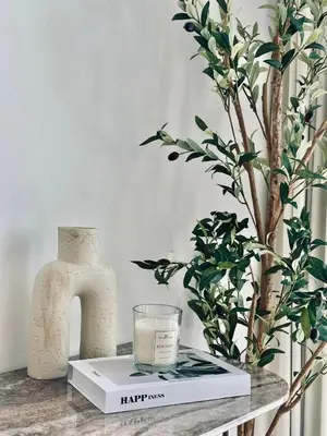 a table with a book and a candle and a vase at Cream Toned 1BR Suite with Parking Pool & Gym in Dubai