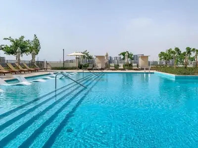a large swimming pool with blue water and chairs at 1BR Little Haven in Collective T1, Dubai Hills in Dubai