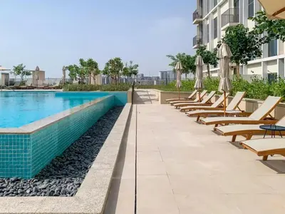 a row of chairs and umbrellas next to a swimming pool at 1BR Little Haven in Collective T1, Dubai Hills in Dubai