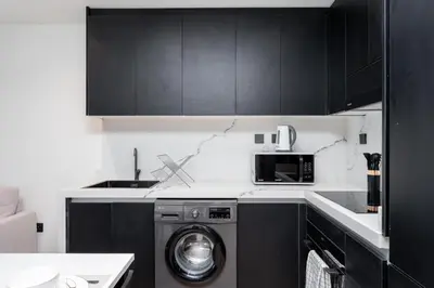 a kitchen with black cabinets and a washing machine at Gala Guests - Elite Sea View Suites Dubai Marina in Dubai