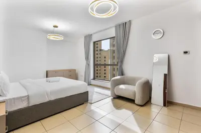 a bedroom with a bed and a chair and a window at Chic 2-bed Oasis with Marina Views Walk to Beach! in Dubai