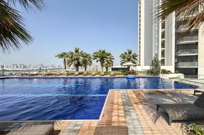 a large swimming pool with palm trees and a building at PVH - Golf Vita - 1BR with Golf Course View in Dubai